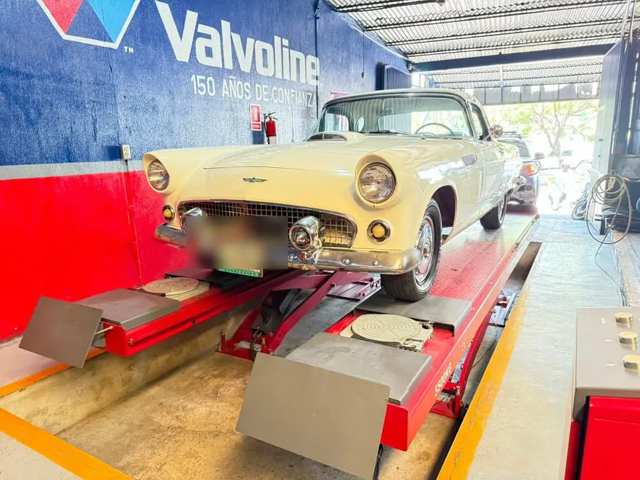 Ford Thunderbird clásico convertible estacionado frente al rótulo de Valvoline del taller