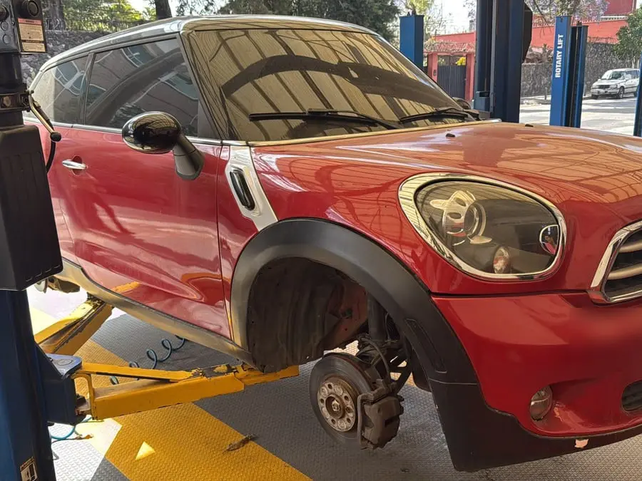 MINI Countryman rojo con la rueda delantera desmontada sobre el elevador del taller