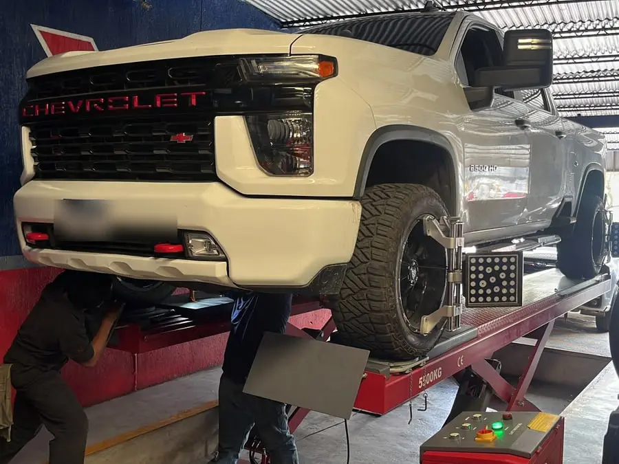 Camioneta Chevrolet Silverado blanca sobre la rampa de alineación con mecánicos trabajando debajo