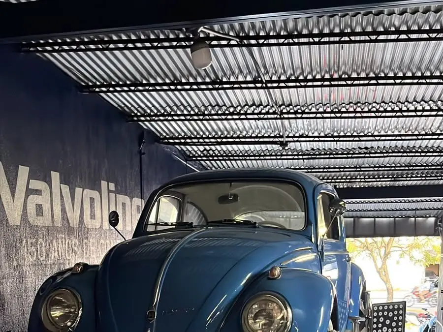 Volkswagen Escarabajo azul de frente bajo el techo del taller, junto al rótulo de Valvoline
