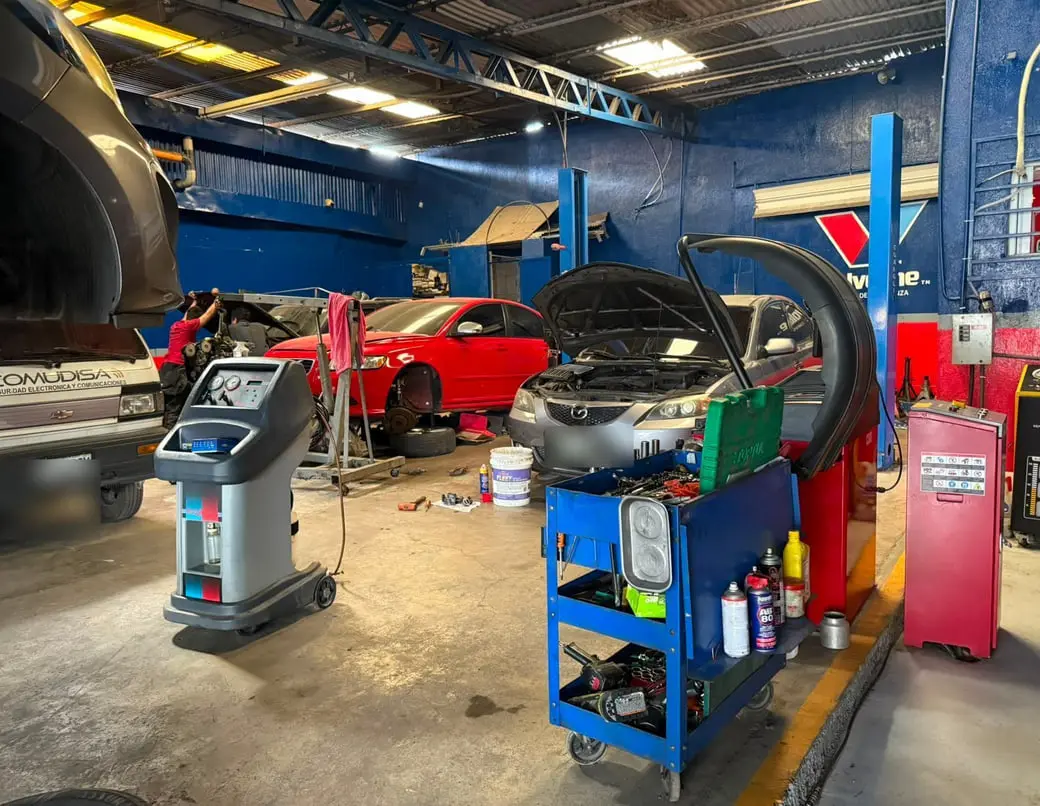 Vehículos en servicio dentro del taller junto a la máquina de recuperación de refrigerante de aire acondicionado