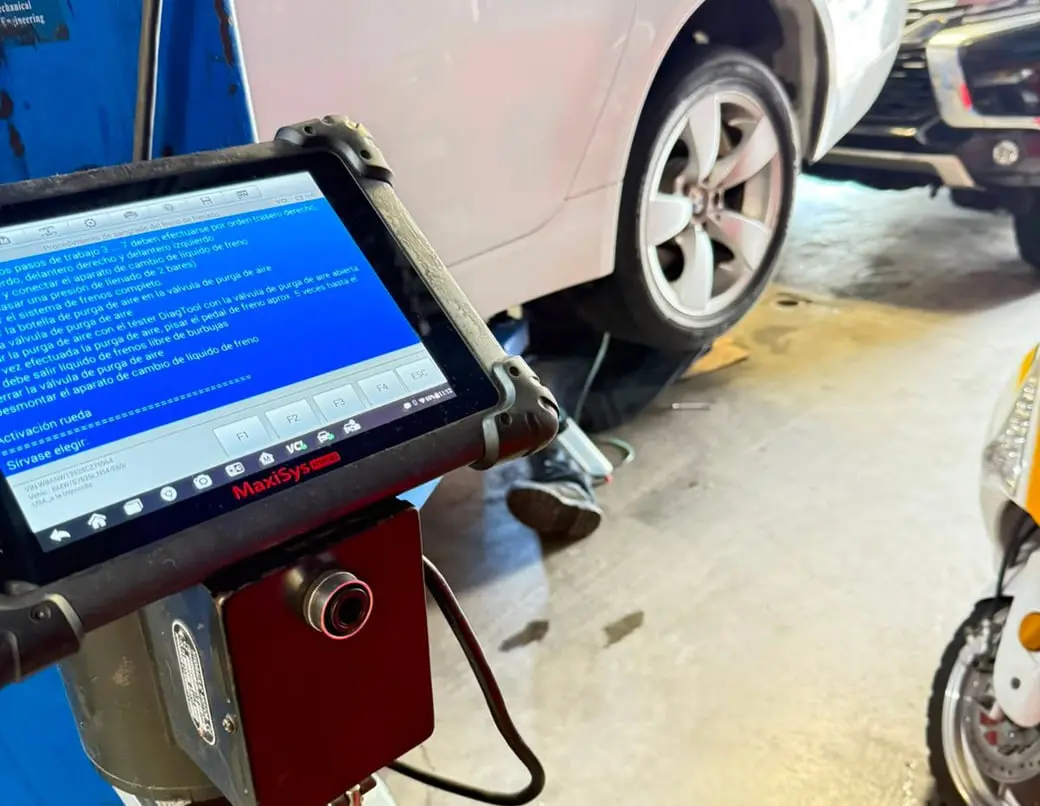 Tableta de diagnóstico automotriz mostrando un procedimiento de purga de frenos junto a un vehículo en el taller