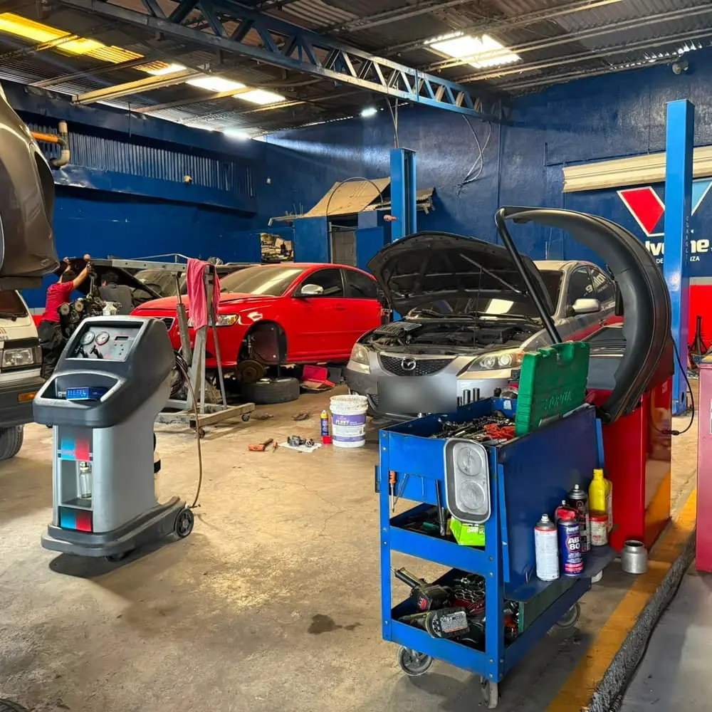 Vista general del taller con vehículos en reparación y la máquina de recuperación de refrigerante de aire acondicionado