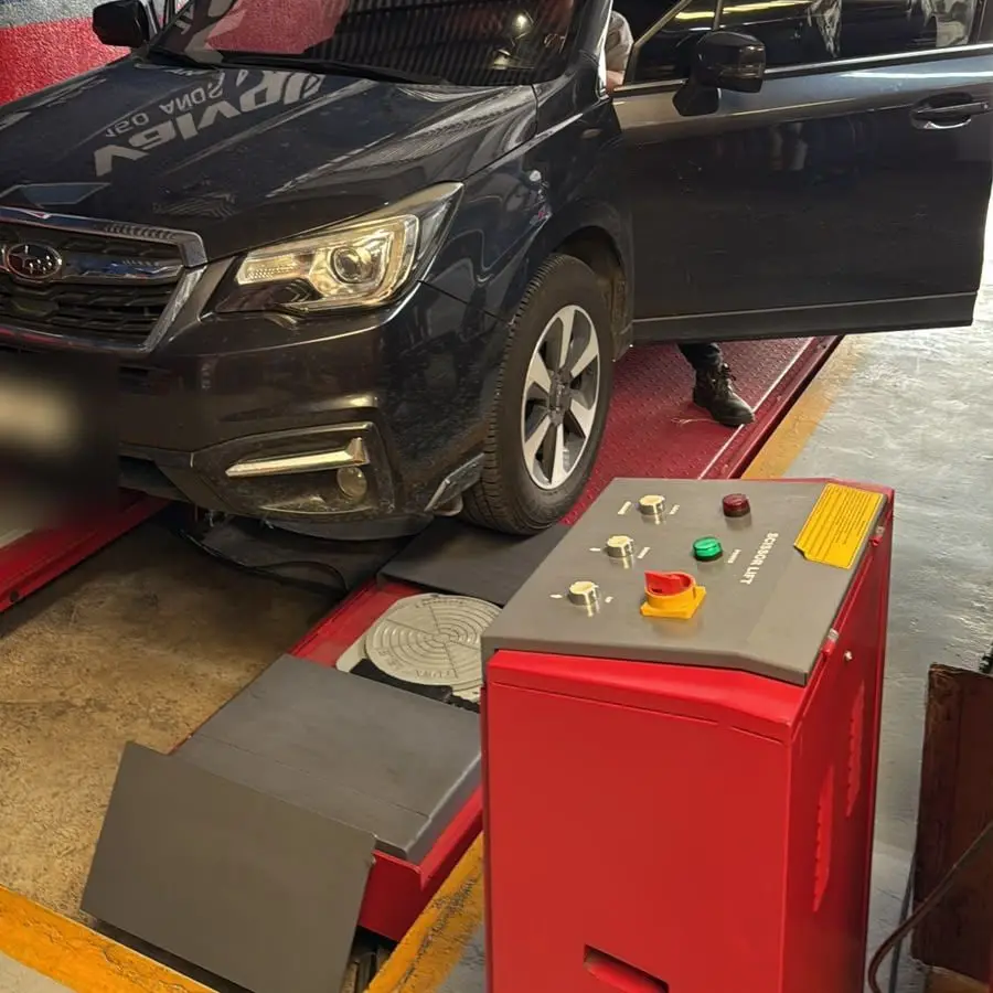 Vehículo sobre el elevador de tijera junto al panel de control del equipo