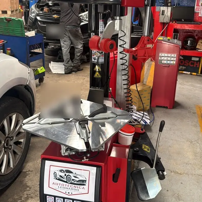 Cabezal de la alineadora junto a la rueda de un vehículo, con un mecánico trabajando en una camioneta al fondo